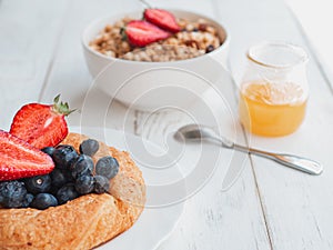 Fresh bagel with berries, oatmeal and honey on a white background. French summer breakfast