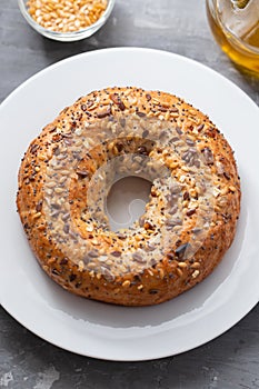 Fresh bagel with seeds on white plate on ceramic background