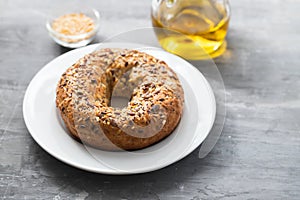 Fresh bagel with seeds on white plate on ceramic background