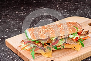 Fresh baguette sandwiches with veal, sliced cheese, tomatoes and fresh lettuce on wooden cutting board. Dark black