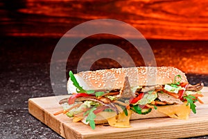 Fresh baguette sandwiches with veal, sliced cheese, tomatoes and fresh lettuce on wooden cutting board. Dark red