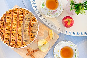 Fresh baked apple pie, cup of tea and flowers on a table