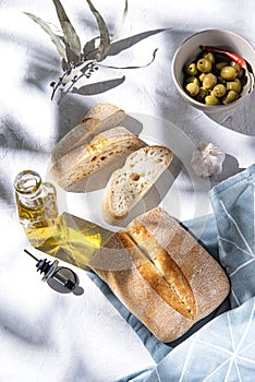 Fresh baked bread lon the table with olives and oil in the morning sunlight