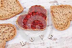 Fresh baked bread in shape of heart with strawberry jam and inscription love. Rustic background