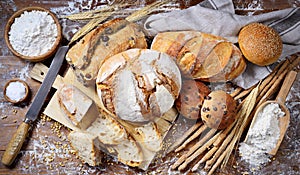 Assorted traditional bread with loaves, rolls and breadsticks on a wooden worktop, top view.