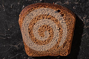 Fresh baked brown bread slice on stone black surface