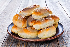 Fresh baked buns sprinkled with sesame seeds in a plate on a wooden table