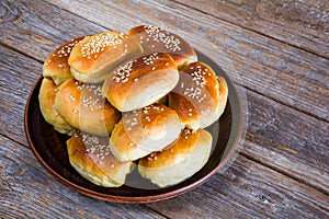 Fresh baked buns sprinkled with sesame seeds in a plate on a wooden table