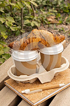 Fresh baked chocolate croissant on Two paper cups with lid for tea to go. Empty paper notebook. Freelancer's place