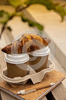 Fresh baked chocolate croissant on Two paper cups with lid for tea to go. Empty paper notebook. Freelancer's place