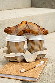 Fresh baked chocolate croissant on Two paper cups with lid for tea to go. Empty paper notebook. Freelancer's place