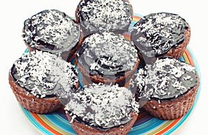 Fresh baked chocolate muffin with desiccated coconut on colorful plate. Delicious dessert