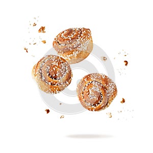 Fresh baked cinnamon buns with crumbs flying falling isolated on white background