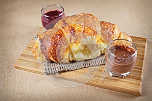 Fresh baked croissants with raspberry jam and chocolate on wooden chopping board