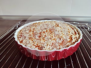 Fresh baked golden apple pie in red dish in oven at kitchen