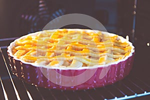 Fresh baked golden apple pie in red dish in oven at kitchen