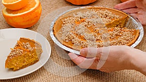 Fresh baked homemade pumpkin pie decorated with crushed nuts and orange zest. Woman hands serving pie on a plate