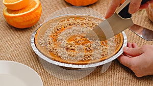Fresh baked homemade pumpkin pie decorated with crushed nuts and orange zest. Woman hands serving pie on a plate