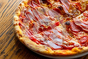 Fresh baked homemade sliced pizza with cheese and ham topping on wooden background.