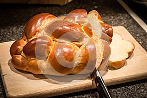 Loaf of challah bread being cut with knife.