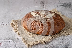 Fresh baked loaf of spelt sourdough bread with crushed hemp seeds is decorated with cannabis leaf made of flour on linen towel on