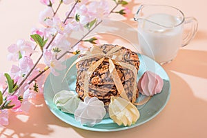 Fresh baked oatmeal crispy cookies on a blue plate on a background of peach color, milk, French multi-colored meringues. Delicious