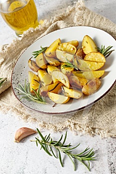 Fresh baked potatoes with olive oil, rosemary and garlic on vintage plate closeup over beige linen towel