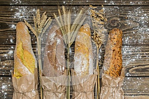 Fresh baked rustic bread loaves in paper bags on dark wood background