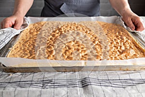 Fresh baked sponge cake for making swiss roll on a baking sheet is held by a womans hand