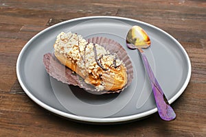 fresh baked sweet creamy eclair sweet dessert on plate with spoon, kitchen wooden table, sugar food, utensils dishware, home