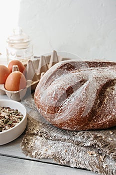 fresh-baked wholegrain round bread  seeds  eggs  whisk  spilled cereal on white wooden kitchen table  vertical food content  ready