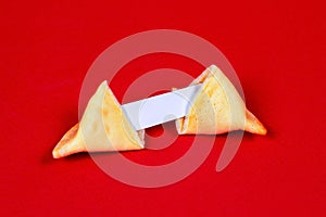 Fresh baked yellow Chinese fortune cookies with white blank note inside on red background.