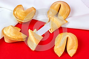 Fresh baked yellow Chinese fortune cookies with white blank note inside on red background.