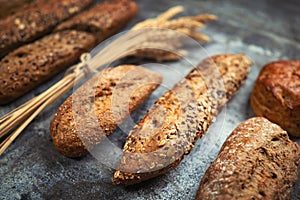 Fresh bakery food. Crusty loaves of mixed breads and buns and ears of wheat on rustic table background.