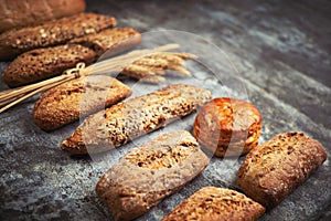 Fresh bakery food. Crusty loaves of mixed breads and buns and ears of wheat on rustic table background. Shallow DOF and copy space