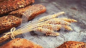 Fresh bakery food. Crusty loaves of mixed breads and buns and ears of wheat on rustic table background. Shallow DOF and copy space