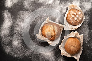 Fresh bakery food, rustic crispy loaves of bread and buns on black stone background with flour, homemade baking, top