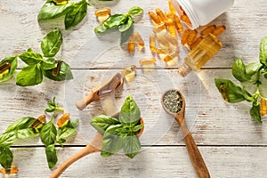 Fresh basil leaves with capsules and essential oil on wooden table