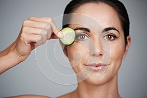 Fresh beauty secrets. Studio shot of a beautiful mid adult woman holding a slice of cucumber to her face.