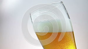 Fresh beer with foam into drink pint glass with ice frozen drops, shot slow motion on white background, fun and nutrition