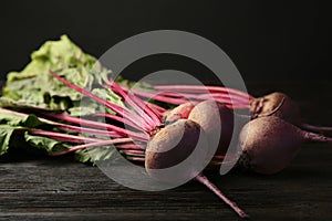 Fresh beets with leaves on dark wooden table against black background