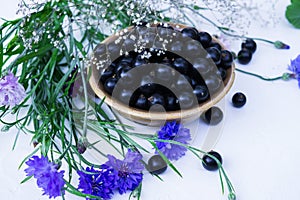 Fresh berries of black currant in a plate on a table together with cornflowers . For a diet and saturation with vitamins