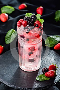 Fresh berries cocktail with raspberry, blackberry, mint and ice in jar glass on dark black background. Summer cold drink