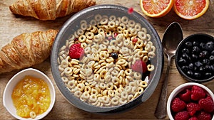 Fresh berries and pomegranate seeds fall into the ceramic bowl filled with cereal rings