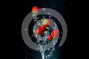 Fresh berries in splashes of water on black background. Juicy strawberries