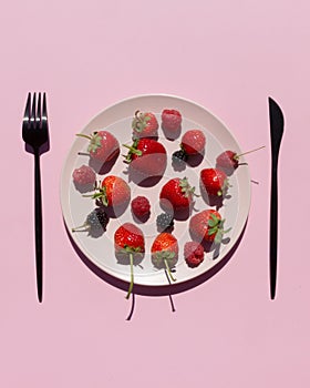 Fresh berries, strawberries, raspberries, blackberries in pink ceramic plate on pink background. Vegetarian or fruitarian diet