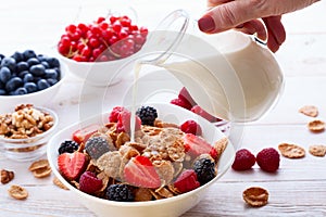 Fresh berries strawberry, raspberries and natural flakes for breakfast, Woman pouring milk into bowl with muesli top