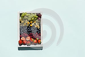 Fresh berries in a wooden white box: strawberries, blueberries, raspberries, grapes and physalis are in a box for sale or delivery