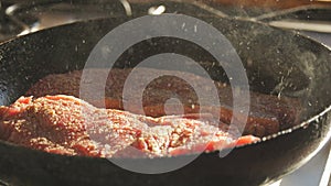 A fresh big red piece of beef is being prepared for frying a steak in a pan. Steak slow motion. Splashes of grease and