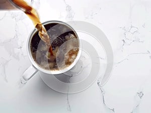 Fresh black coffee being poured into white mug on marble tabletop